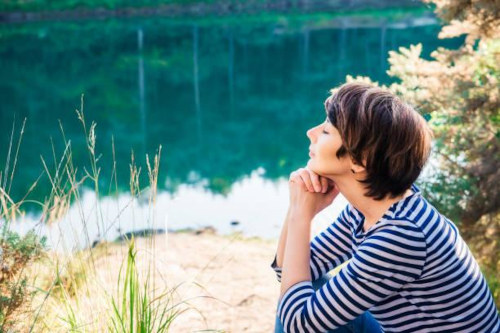 Woman sitting next to a lake, chin on hands, contemplating.
