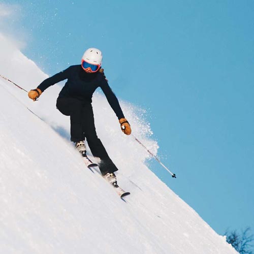A skilled skier going down a steep hill with bright blue sky.