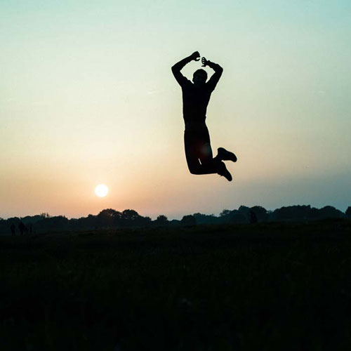 Silhouette of man jumping high against a beautiful sunrise.